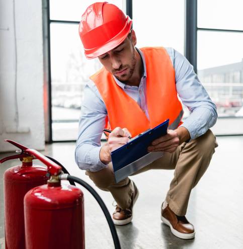 serious fireman in helmet writing on clipboard while checking extinguishers